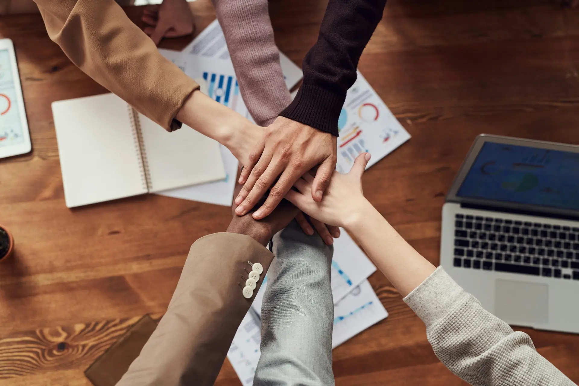 alt="Diverse professionals unite for teamwork around a wooden table with laptops and documents."